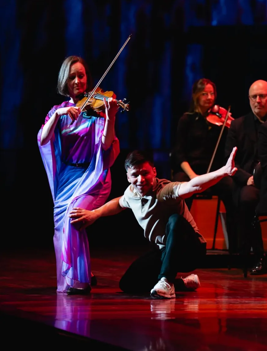 Bao dancing on stage with a violinist, orchestra in the background