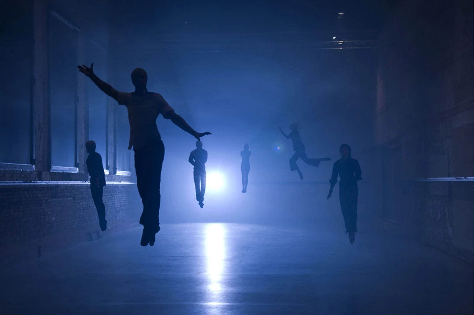 Silhouettes of people in motion in a room, one with arms outstretched